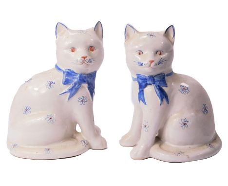 A pair of Rye pottery cats, in seated position wearing blue bows and decorated with flowers against an off white ground, 20cm