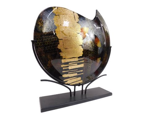 An Oxford art glass, of shaped circular form, decorated with abstract patterns against a mottled black ground, on metal stand