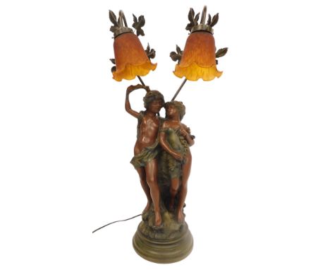 A 20thC painted cast metal figural table lamp, with two amber glass shades, the base modelled as young male and female scanti