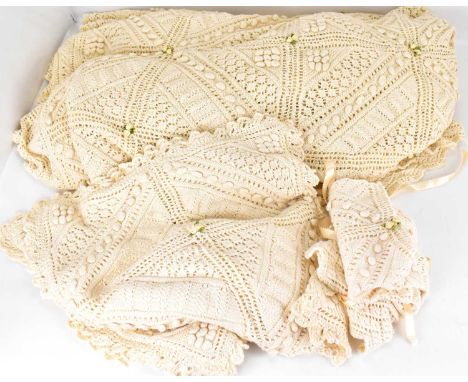 A vintage cream hand-knitted bedspread decorated with satin rosebuds, 244 x 183cm, together with three similar cushion covers