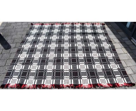 A vintage Welsh wool blanket with repeating black, white and red squares on a grey ground, with red, black and white tassels,
