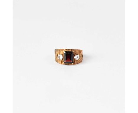 A 1970s 9ct gold ring with claw set cushion cut garnet flanked by two bright white stones, on textured shoulders, size K, app