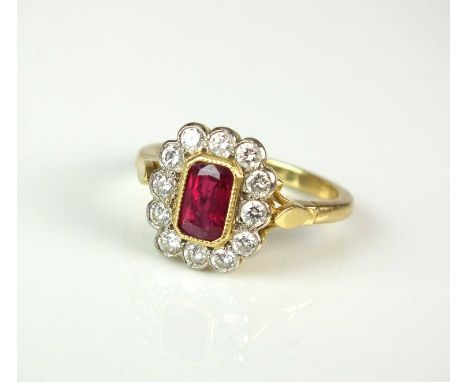 An 18ct gold ruby and diamond cluster ring, designed as a central trap cut ruby collet set in yellow gold within a border of 