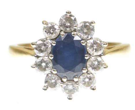 A sapphire and diamond cluster ringThe oval shape sapphire to a round brilliant cut diamond surround, modelled in unmarked pr