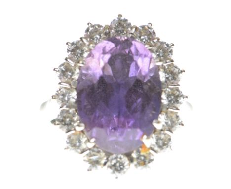 An amethyst and diamond cluster ringCentering an oval shape amethyst within a round brilliant cut diamond surround, modelled 