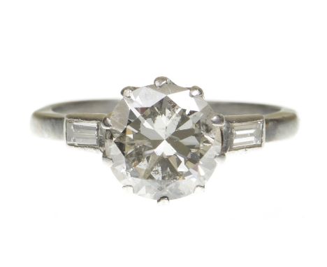 A diamond single stone ringThe round brilliant cut diamond, claw set, flanked by baguette cut diamond shoulders, modelled in 