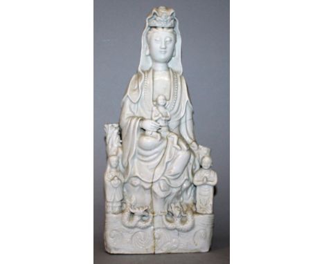 A CHINESE KANGXI PERIOD BLANC-DE-CHINE PORCELAIN FIGURE OF GUANYIN, a child in her lap, seated above waves and dragons flanke