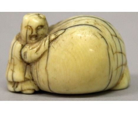 A JAPANESE EDO PERIOD IVORY NETSUKE, carved in the form of a boy leaning against a large bag, 1.5in long & 0.9in high.