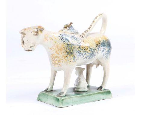 AN EARLY 19TH CENTURY POTTERY COW CREAMER of Prattware type with spongeware decoration in blue and yellow and with calf below