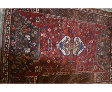 A Persian carpet, the central red field with two geometric urns, flowerhead decoration, flanked by two horizontal panels and 