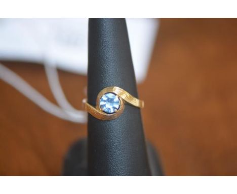 A lady's dress ring set with a single blue stone on yellow metal band marked 750