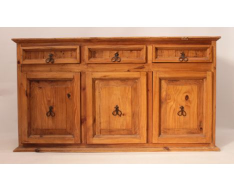 A pine dresser base - the cleated top over three panelled drawers and three panelled cupboards beneath, with wrought iron han