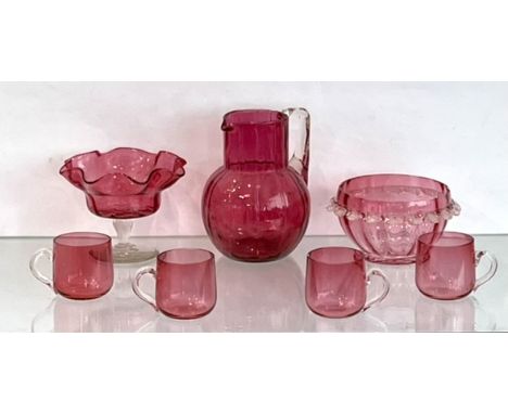 Seven pieces of cranberry glass - including a jug with blown fluted decoration and angular clear glass handle, 16cm high; a p