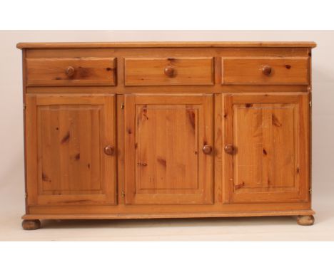 A pine dresser base or side cabinet - the moulded top over three drawers and three panelled cupboards beneath, on bun feet. (