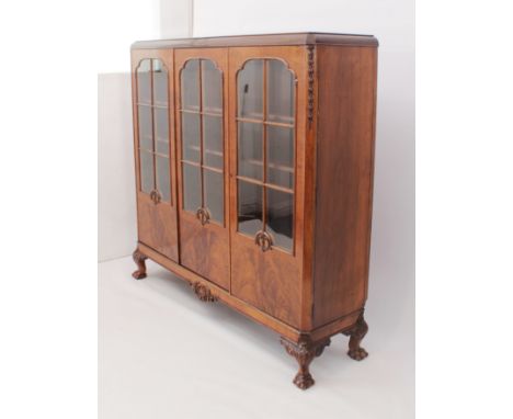 A 1930s walnut glazed bookcase - the convex moulded top with scale carved angles, over three six-pane arched astragal glazed 