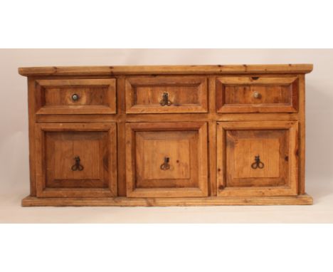 A pine dresser base - the cleated top over three panelled drawers and three panelled cupboards beneath, with wrought iron han