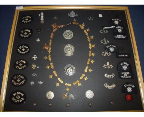 Framed and mounted display of St Johns Ambulance badges, medals etc including cloth arm badges for various Counties, lapel ba