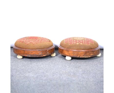 A pair of footstools, walnut upholstery with needlepoint upholstery, each having three fluted ceramic feet.