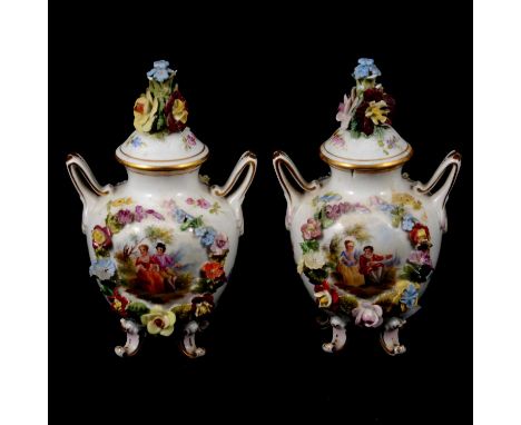 Pair of Continental porcelain lidded vases, twin handled form, painted vignettes within floral encrusted borders, 15cm.Qty: 2