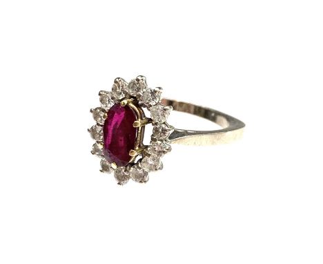 An 18ct white gold ring set an oval ruby of approximately 1ct within a halo of 14 bright brilliant-cut diamonds Hallmarked 19