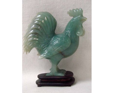 A Chinese celadon jade carved model of a standing cockerel 13cm high on a carved hardwood stand