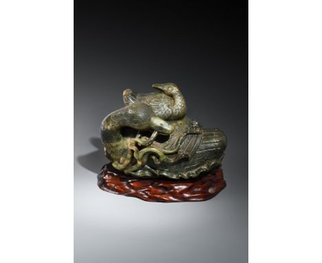 A large Chinese spinach jade 'boulder' carving of a 'duck', Qing Dynasty, holding a lotus flower in her mouth, the interior h