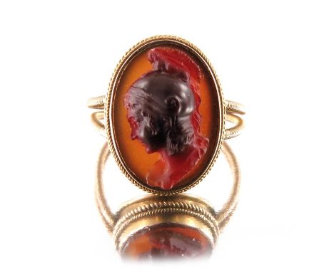 A Revivalist yellow metal and carved carnelian ring, in the style of Castellani, the central stone modelled in relief as a Ro