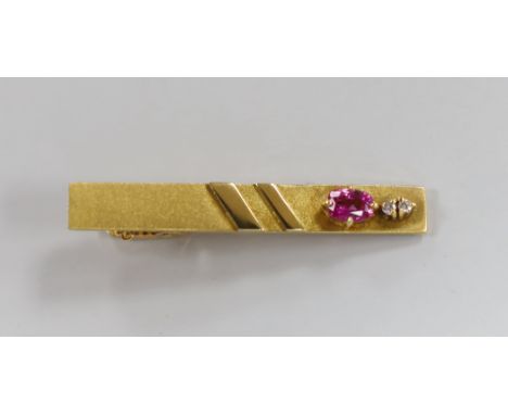 A modern 18k, ruby and diamond set three stone tie clip, 47mm, gross weight 7.7 grams.