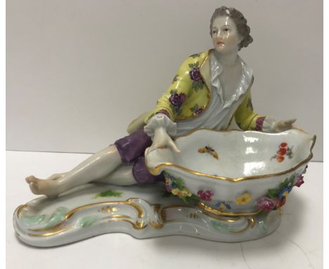 A Meissen figural salt as a man in 18th Century dress beside a large boat shaped dish with floral encrusted decoration, bears