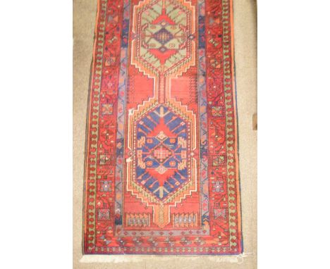 Middle Eastern wool runner, brick red field with triple pole medallion, within foliate border, 74cm x 288cm