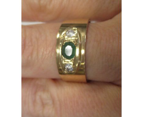 An emerald and diamond ring, the central oval emerald set to either side with a round brilliant cut diamond, all in rubover s