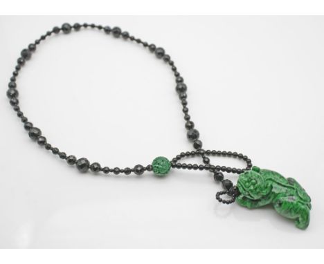 Kette. Facettierte Kugeln aus schwarzem Onyx oder Glas. Figürlicher Anhänger in Form eines Qilin aus grünem, schwarz gemasert