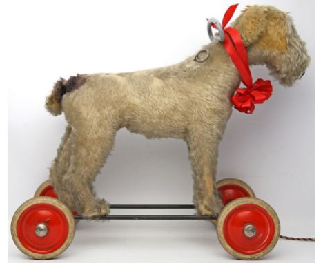 Reittier "Terrier". Verschiedenfarbiger Mohair, teils abgenutzt. Schwarz gelacktes Eisengestell, rote Metallräder mit Gummibe