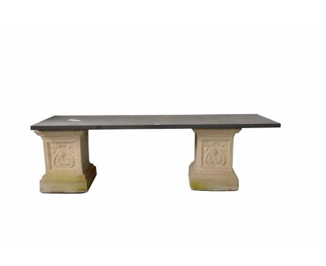 A decorative stone composite garden bench, with slate slab seat pad, raised on two stone composite pedestals, with plant and 