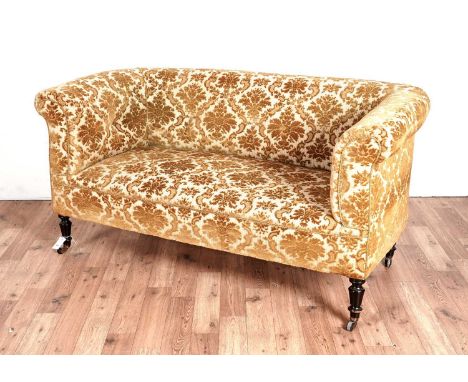 An late Victorian button back sofa with scroll over arms, raised on turned and ebonised legs terminating in ceramic castors, 