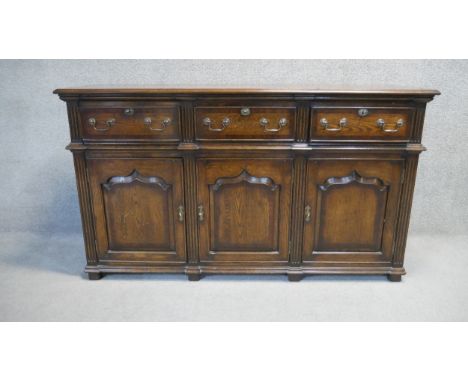 A mahogany crossbanded sideboard in the antique country oak style fitted with lift out cutlery drawers above arched fielded p