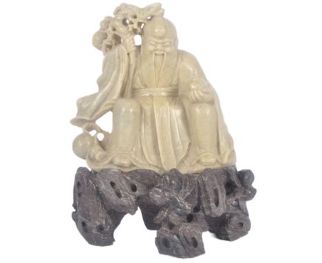 A 20th Century hand carved Chinese Oriental soapstone figurine depicting an Immortal. The figure modelled seated with staff &