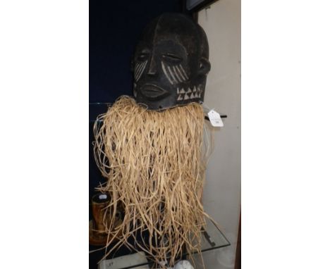 A carved hand painted tribal 'Helmet' mask with raffia fringe