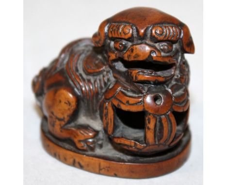 A JAPANESE CARVED WOOD NETSUKE OF A BUDDHISTIC LION, it's head resting on a pierced ribboned ball, 1.75in wide & 1.6in high.