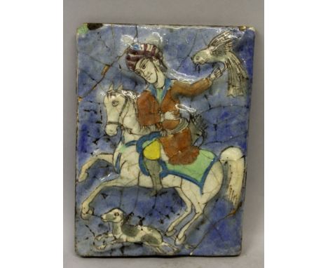 A 19TH/20TH CENTURY PERSIAN MOULDED CERAMIC TILE, decorated with a mounted hunter supporting a hawk, a hound running at the h