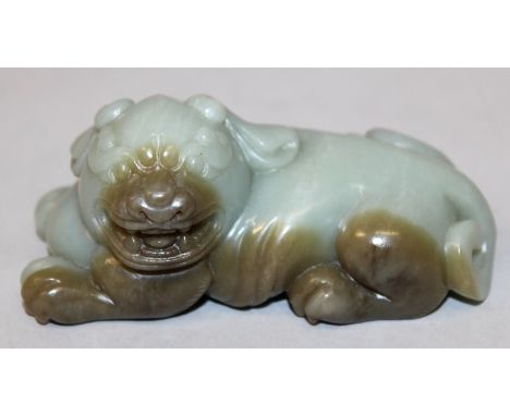 A CHINESE JADE-LIKE MODEL OF A BUDDHISTIC LION, lying down with ferocious expression and turned head, 4in long.