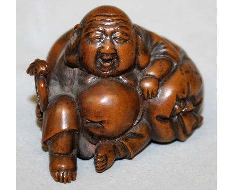 A JAPANESE MEIJI PERIOD CARVED WOOD NETSUKE OF HOTEI, the deity holding a fan and leaning back against his bag, 1.9in wide & 