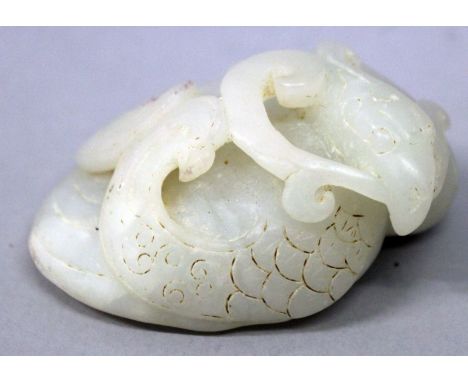 A CHINESE WHITE JADE-LIKE MODEL OF A COILED PHOENIX, clasping a foliate scroll in its beak, 2.7in wide x 1.3in high.