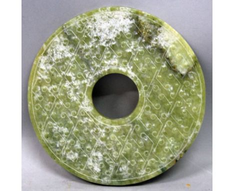 A CELADON JADE-LIKE BI DISC, of archaic form and with formal stud decoration, the predominantly green stone with white and ru