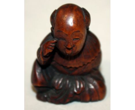 A JAPANESE MEIJI PERIOD WOOD NETSUKE OF A SEATED BOY, with protruding tongue, and holding an oni mask behind his back, 1.6in 