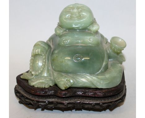 AN EARLY 20TH CENTURY CHINESE CARVED DARK GREEN BOWENITE FIGURE OF BUDAI, together with a fitted wood stand, the deity seated