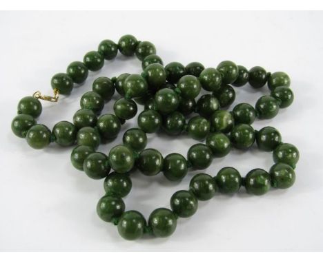 A string of sixty five jade beads, on a yellow metal clasp, stamped 9ct