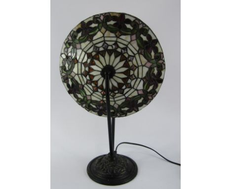 A Tiffany style table lamp, the circular spinning glass shade with floral decoration, raised on cast metal 'v' support and em