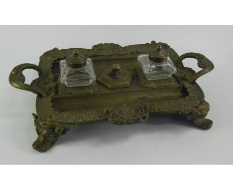 A Continental brass desk stand, of twin handled, rectangular form, embossed with rococo scrolls and leaves, with a pair of gl
