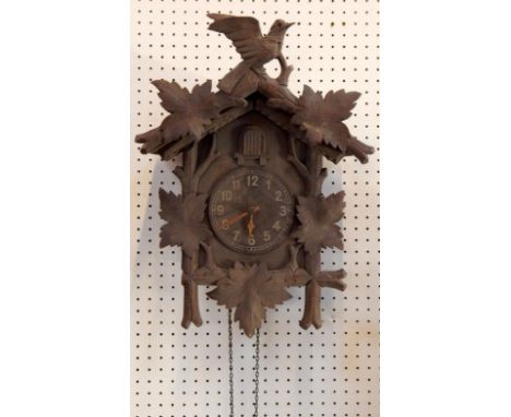 A Black Forest cuckoo clock, traditionally carved with a bird and leaves, circular dial bearing Arabic numerals, two train mo